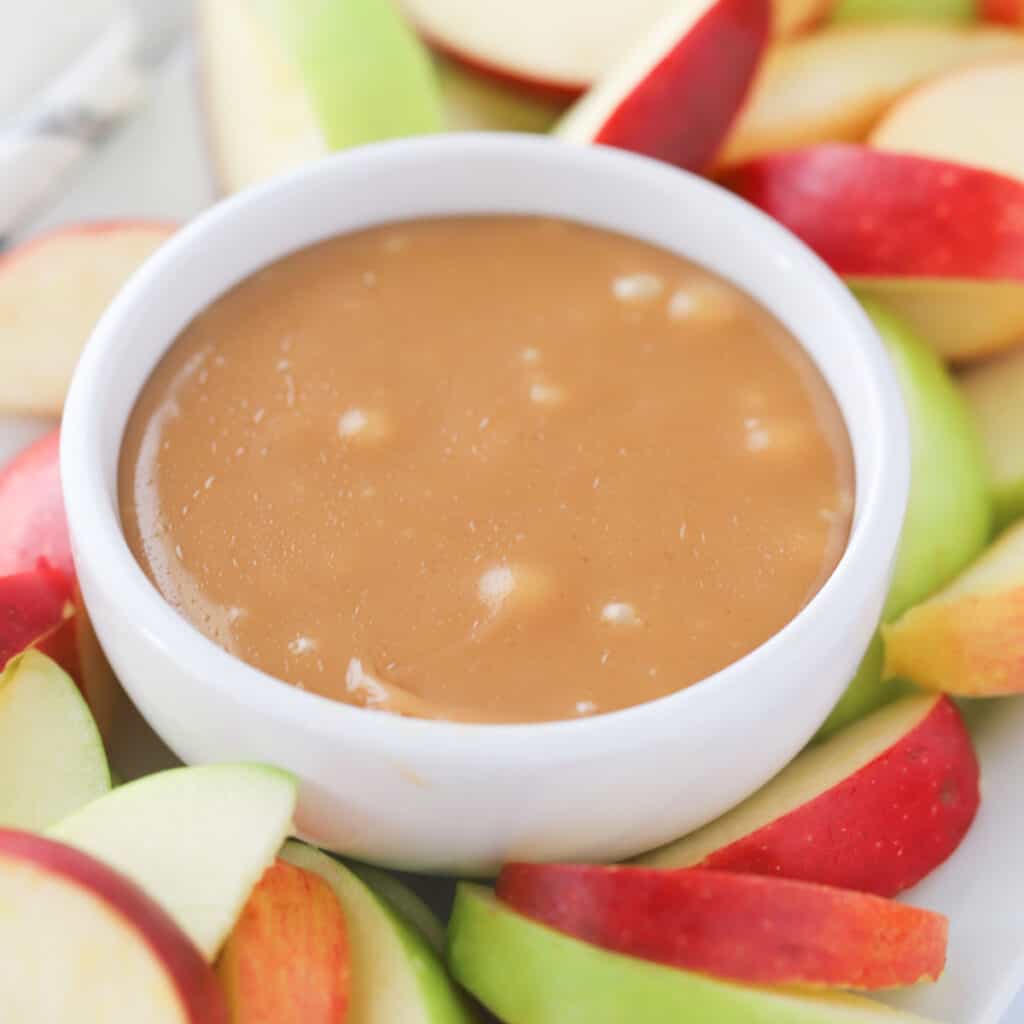 A white ramekin full of caramel with sliced apples around it. Easy caramel dessert. Caramel treat recipes.