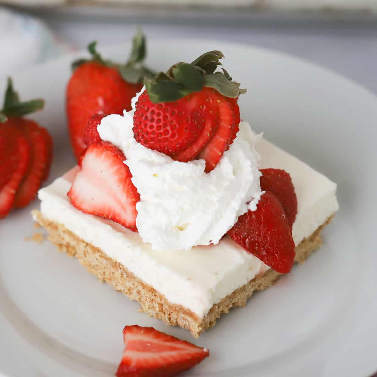 no bake cheesecake bars served with strawberries and whipped cream topping