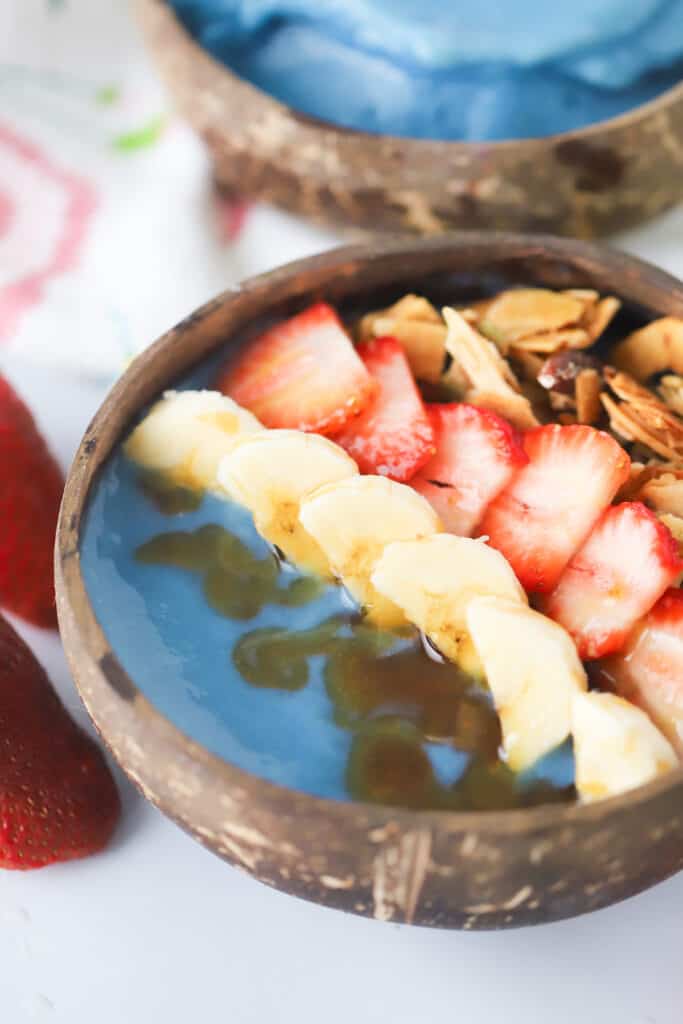 A blue smoothie bowl topped with honey, fresh fruit and granola.