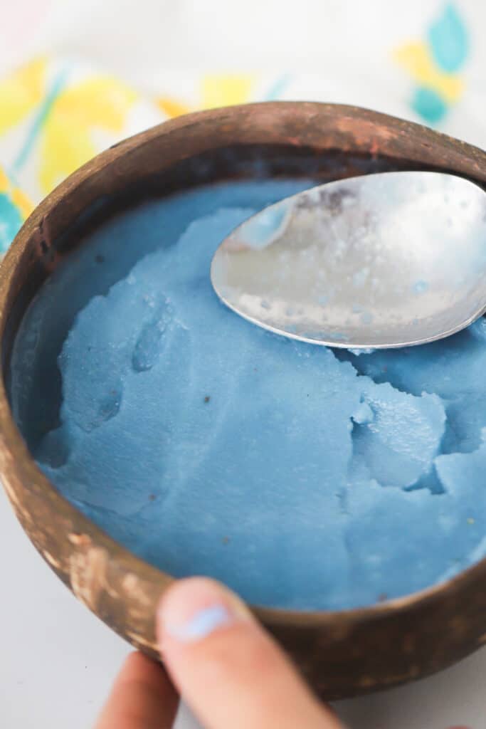 A Blue Smoothie Bowl being pressed into a wooden bowl with a spoon.