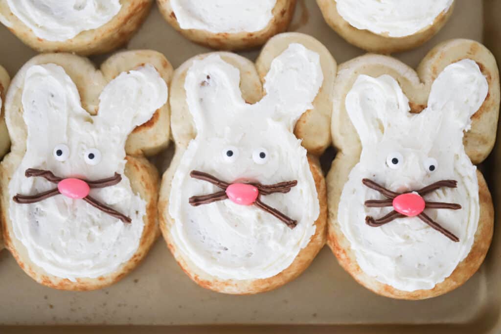 Cinnamon roll bunnies on a baking sheet topped with frosting and decorated with candy and frosting. easter bunny rolls, cinnamon bunnies, bunny biscuits, cinnamon bunny, easter bunny breakfast. 