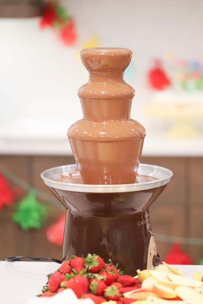 A chocolate fountain on a table surrounded by fresh fruit and other items for dipping.best chocolate for a Chocolate fountain, Chocolate fountain recipes. chocolate for fountain 