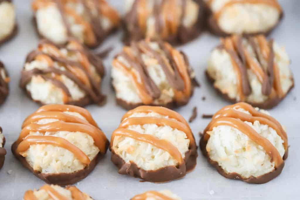 Macaroons dipped in chocolate and drizzled with caramel on a sheet tray.