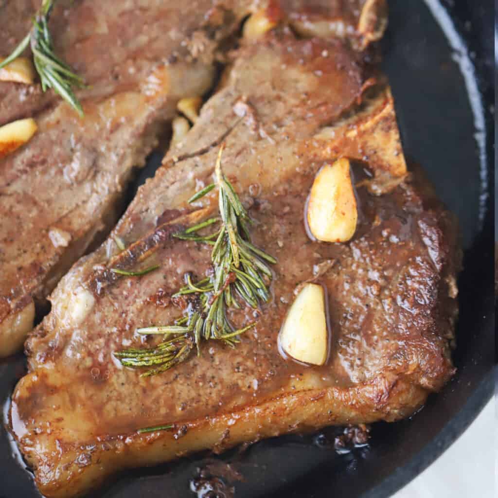 A cast iron skillet with steak covered in garlic and rosemary. family Valentine dinner ideas. 