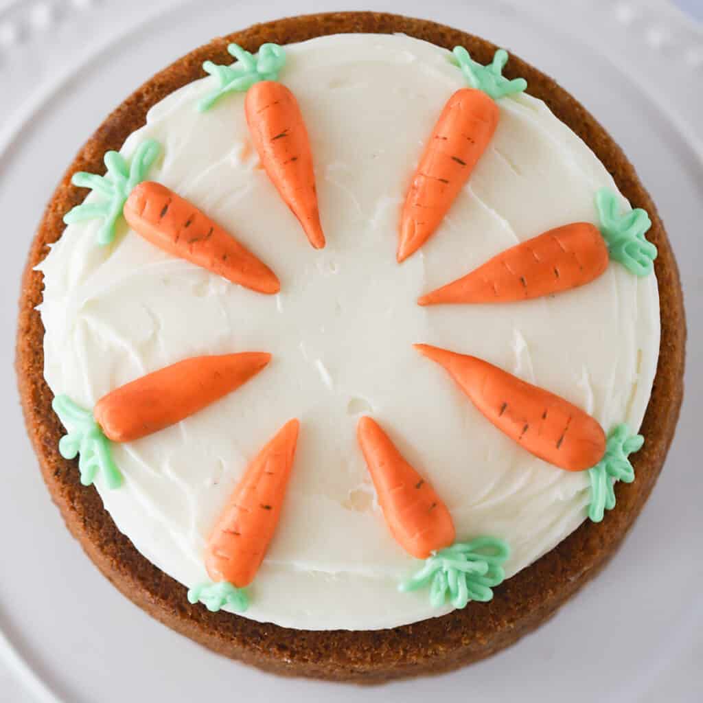 Photo of a decorated carrot cake from above, frosted with cream cheese frosting and carrot decorations.