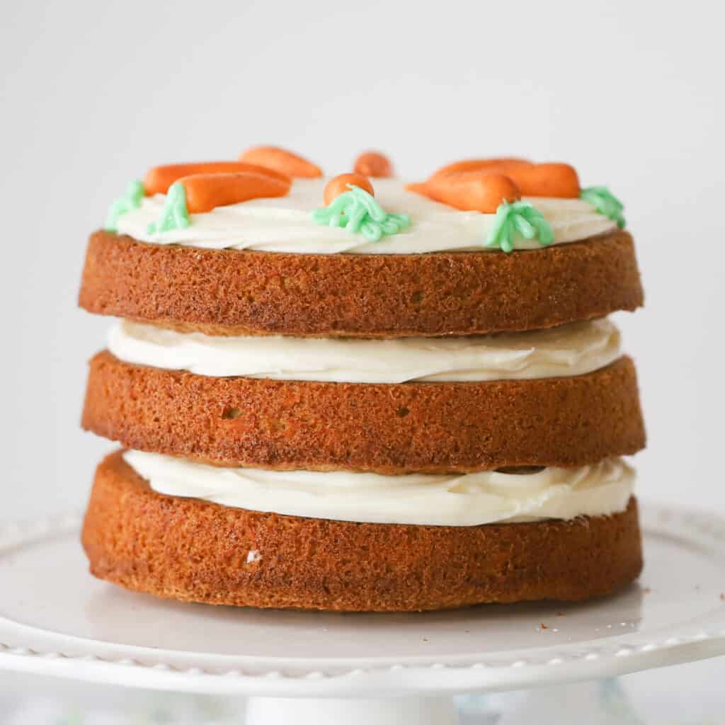 A naked carrot cake made with three layers of carrot cake filled with cream cheese frosting, topped with icing carrots. How to decorate carrot cake.