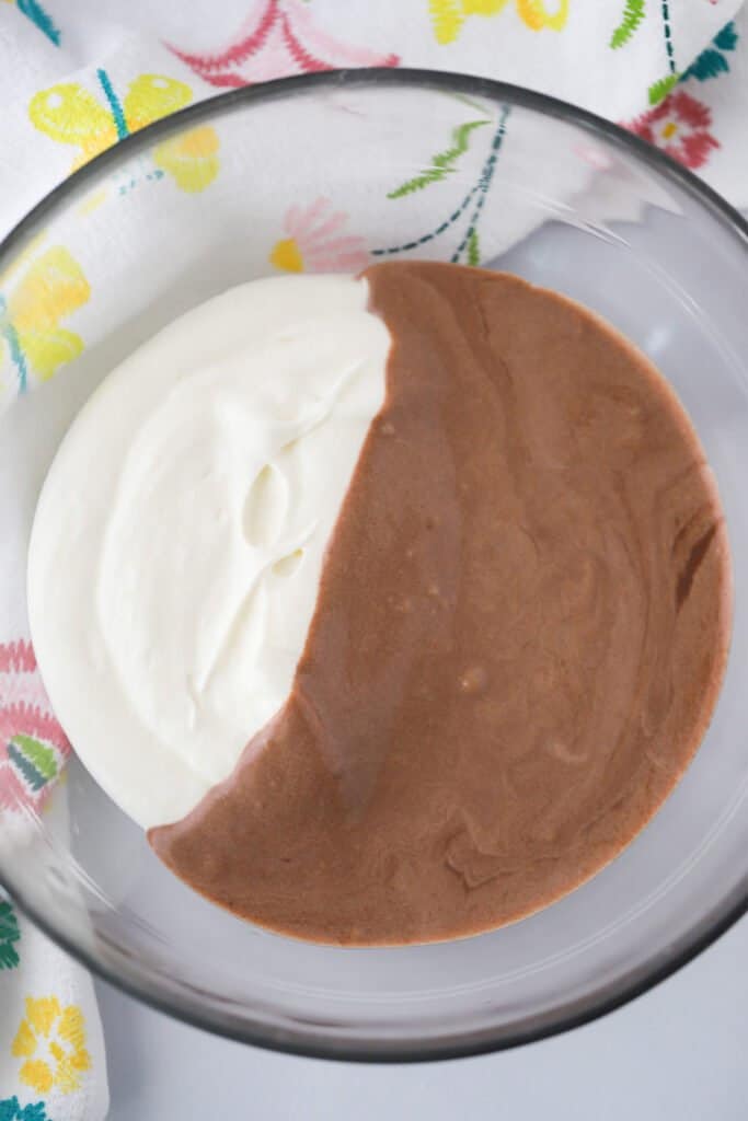 A glass bowl that is filled with half chocolate custard filling for cream puffs and half whipped cream.