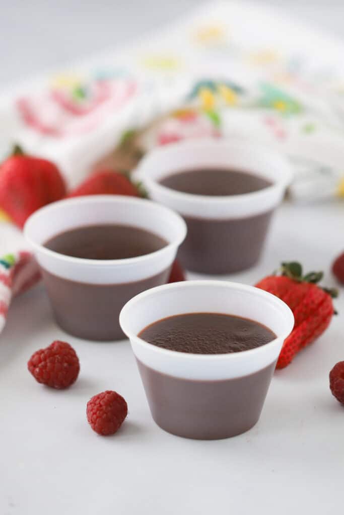 A table with three ramekins full of chilled chocolate pudding surrounded by fresh berries.