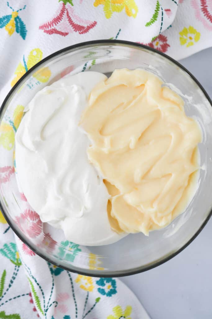 A glass bowl filled with half pastry cream and half whipped cream, about to mix together to make the Cream Puffs filling.