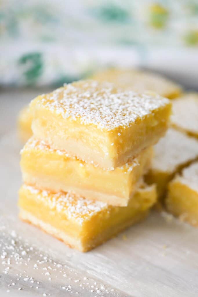 A stack of best lemon bars recipes on a tabletop, dusted with powdered sugar. lemon bars recipe easy; lemon squares.