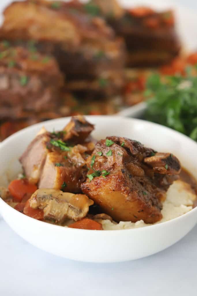 A white bowl full of mashed potatoes and slow cooked short ribs. Recipe short ribs slow cooker. 