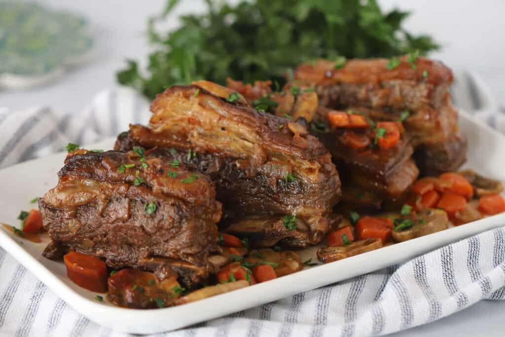 A white serving platter full of Slow Cooker Beef Short Ribs and veggies.