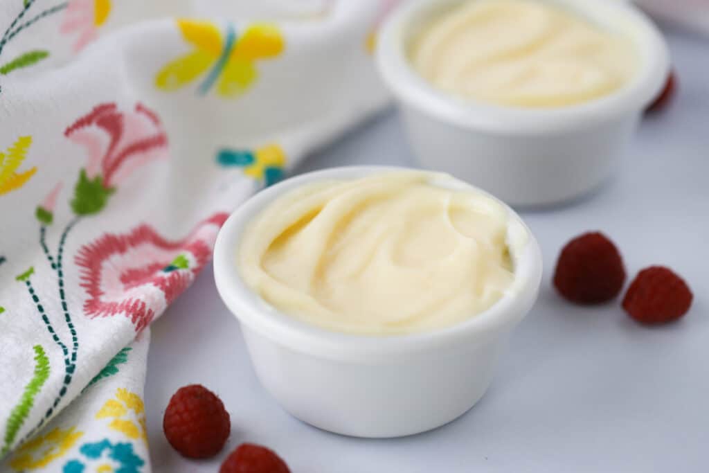 A white ramekin full of vanilla pudding on a table with a decorative napkin and fresh berries.