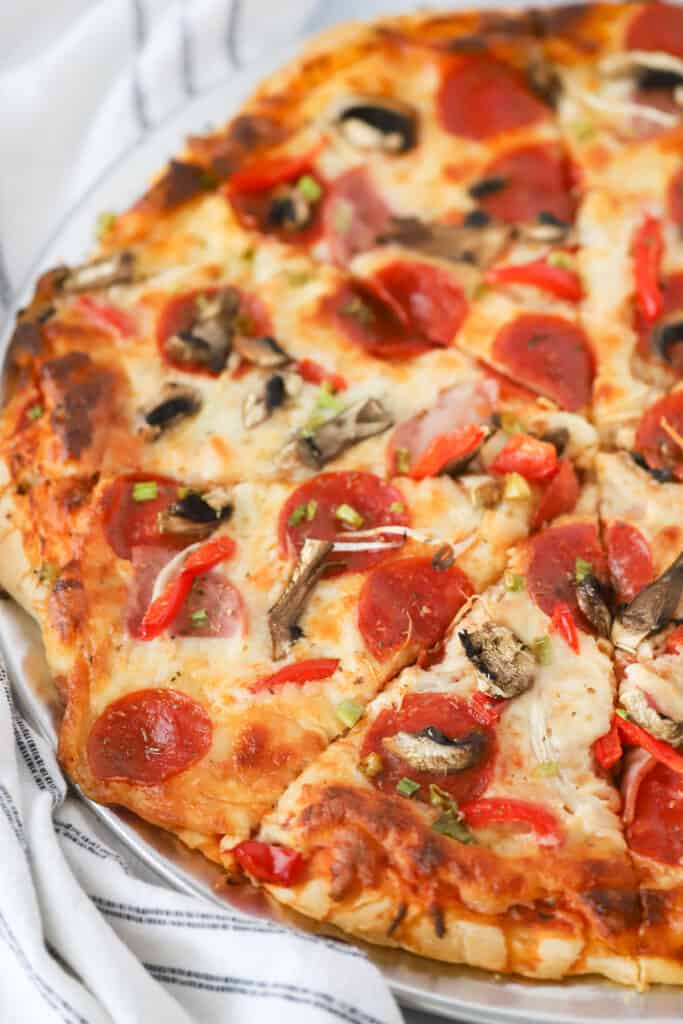 A homemade supreme pizza with pepperoni, mushrooms, peppers and more toppings cut into slices.