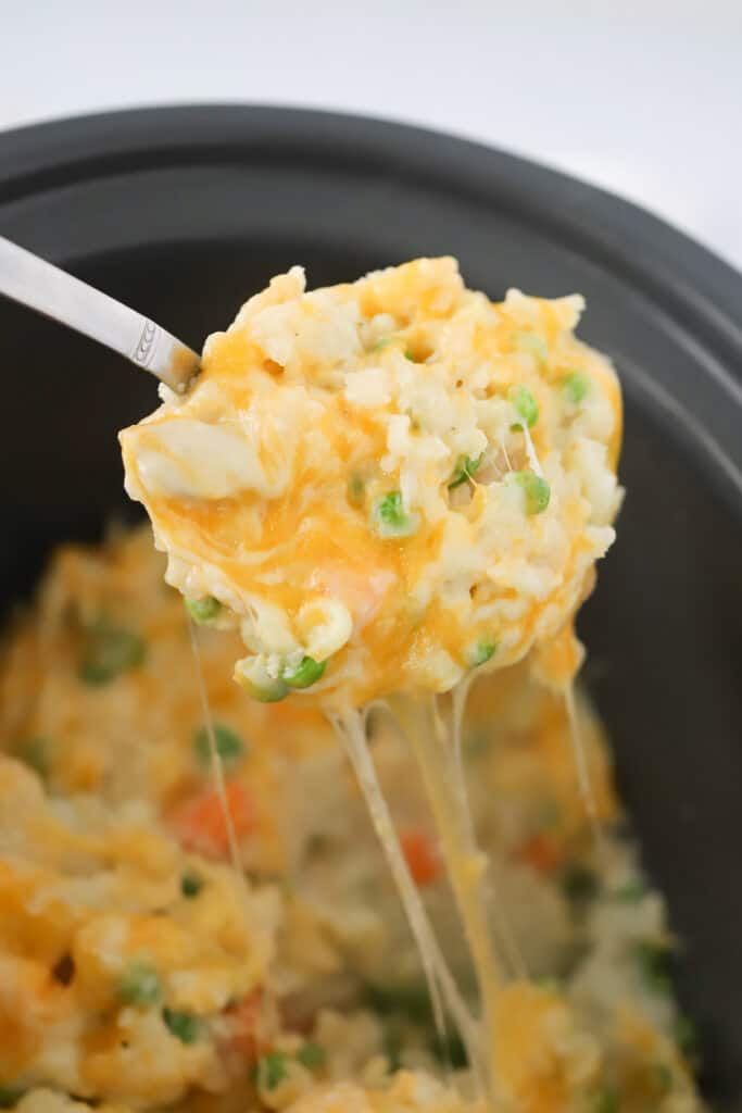 A ladle pulling up a portion of Crockpot Cheesy Chicken and Rice.