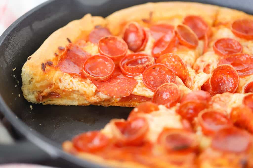 Pizza topped with pepperoni and baked in a skillet with a slice removed.