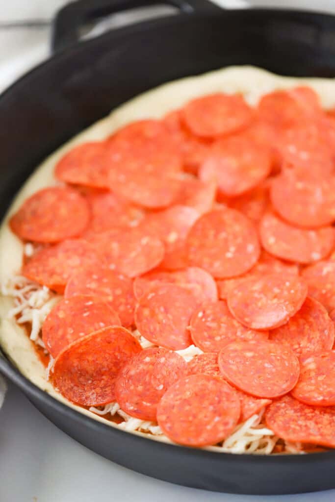 Cast iron pan pizza dough in the pan topped with pepperoni and ready to bake.