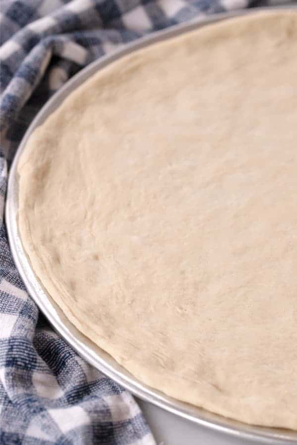 Fresh pizza dough stretched onto a round pizza pan ready to top.