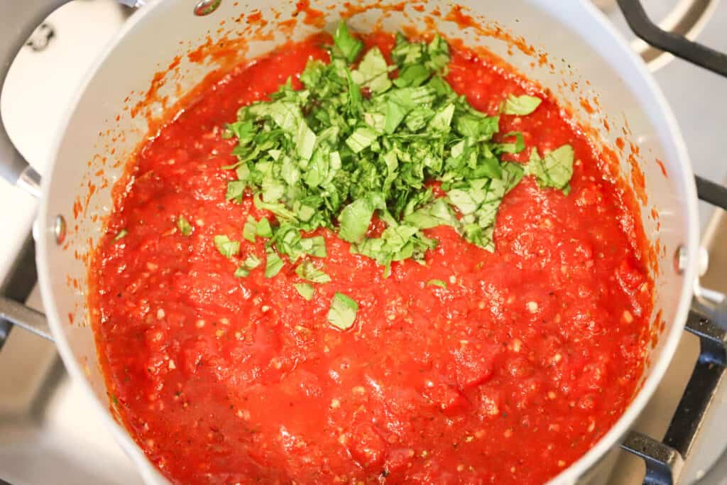Homemade pizza sauce in a pot topped with a pile of chopped fresh basil. Easy pizza sauce recipe. Recipe homemade pizza sauce. Pizza sauce recipe quick.