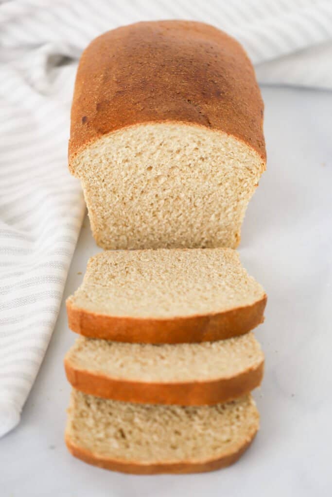 A loaf of Whole Wheat Bread on a counter with a few slices laying down. homemade whole wheat bread, wheat vs white bread, how to make wheat bread at home.