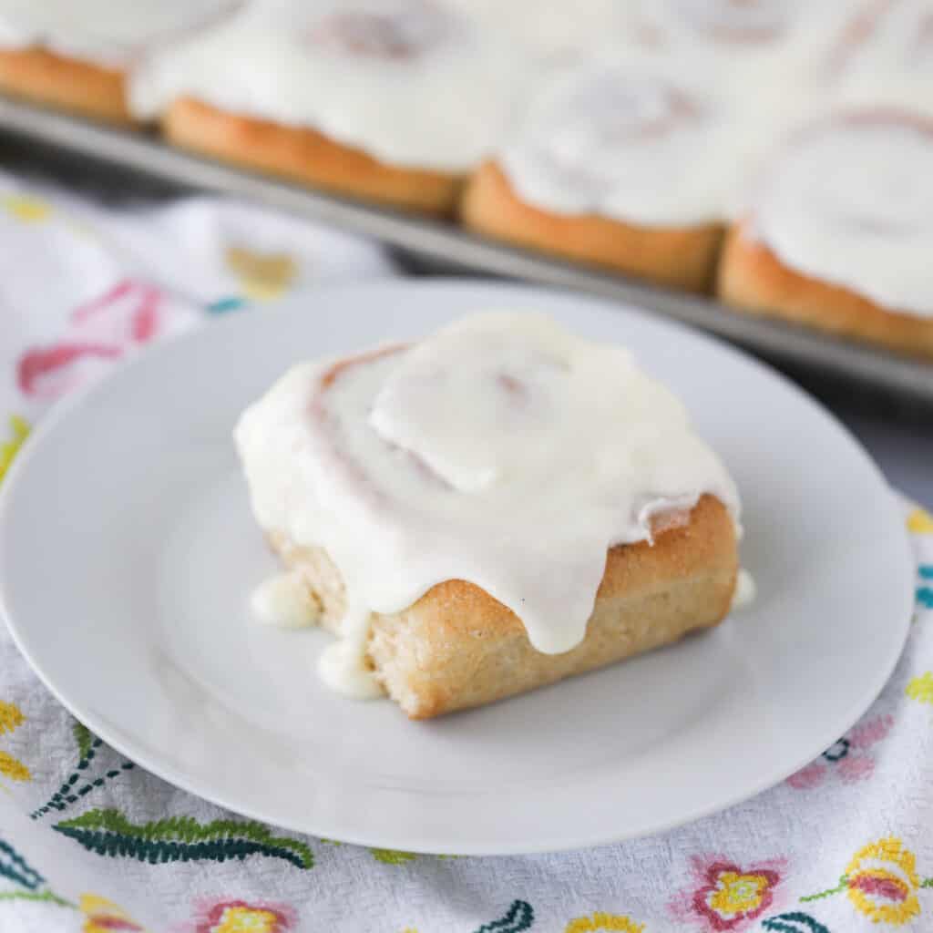 A cinnamon roll on a white plate topped with cinnamon roll frosting.