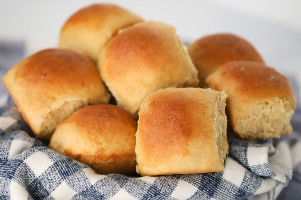 A serving dish lined with a kitchen towel and filled with dinner rolls.