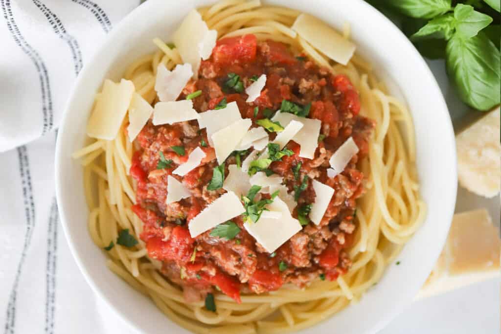 A bowl of spaghetti topped with meat sauce for spaghetti, grated Parmesan cheese and fresh herbs.