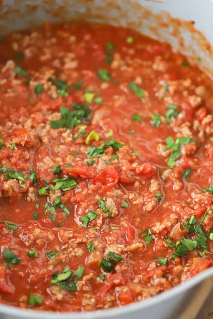 A large saucepan full of meat sauce for spaghetti, topped with fresh green herbs.
