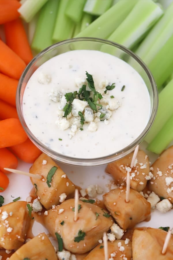 Buffalo chicken bites stuck with toothpicks, surrounded by ranch dressing, carrots and celery sticks.