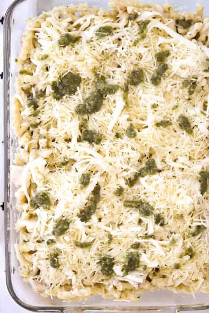 A baking dish layered with pasta, chicken, cheese and pesto ready to bake.