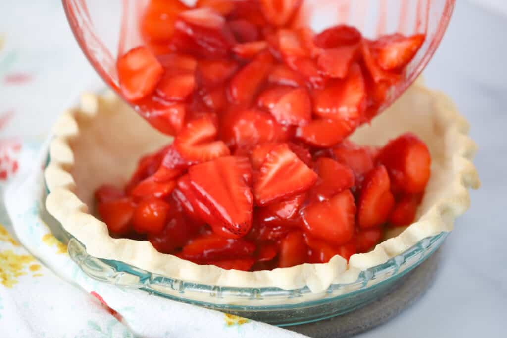 Strawberry filling being added into a fresh pie crust.