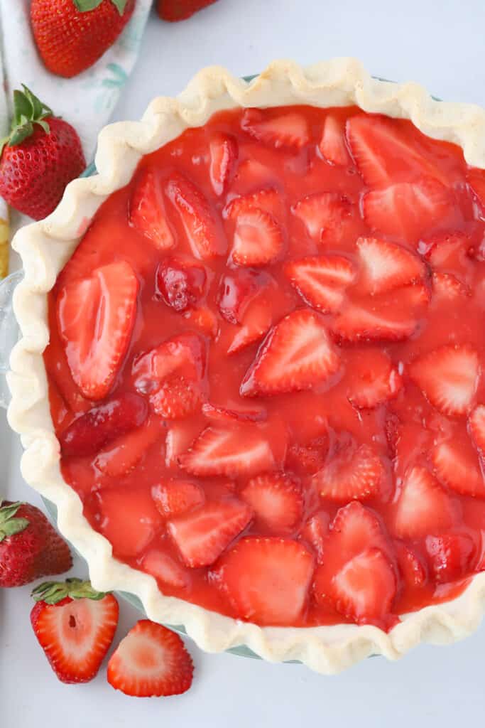A strawberry pie made with fresh strawberries on a table surrounded by more fresh strawberries.