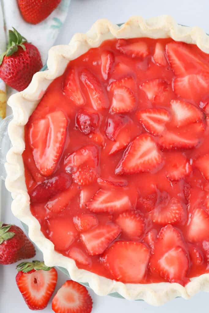 A Fresh Strawberry Pie with a crimped pie crust surrounded by fresh strawberries on a table.