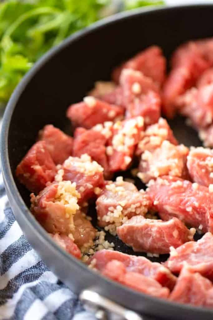 A skillet full of garlic steak bites covered in minced garlic, beginning to cook.