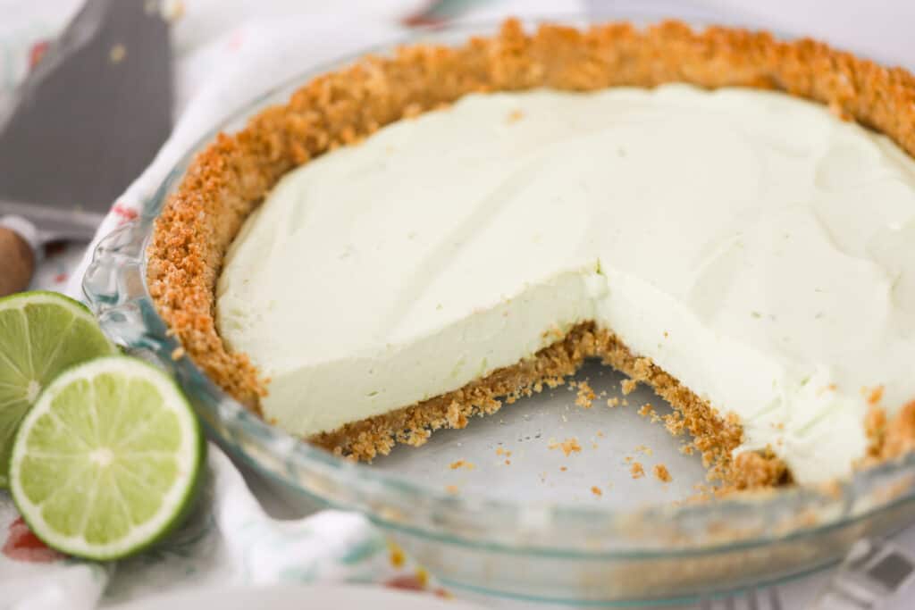 A key lime pie on a table with a large slice removed.
