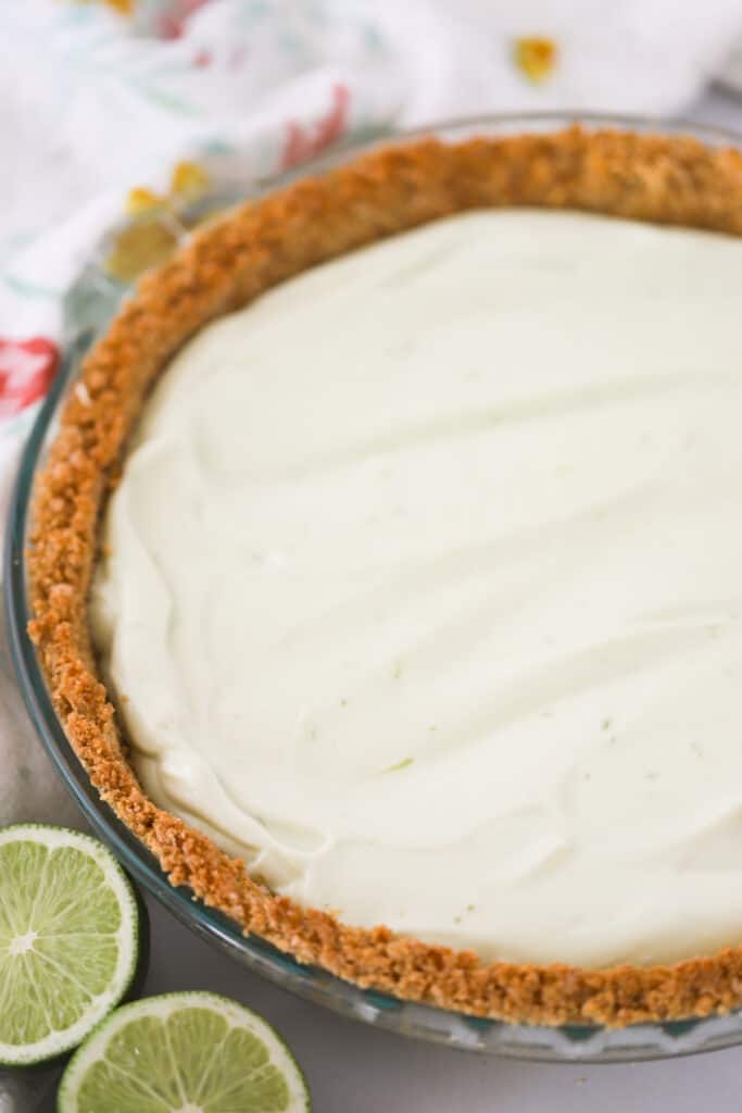 A pie plate with a key lime pie in a graham cracker crust sitting on a table.