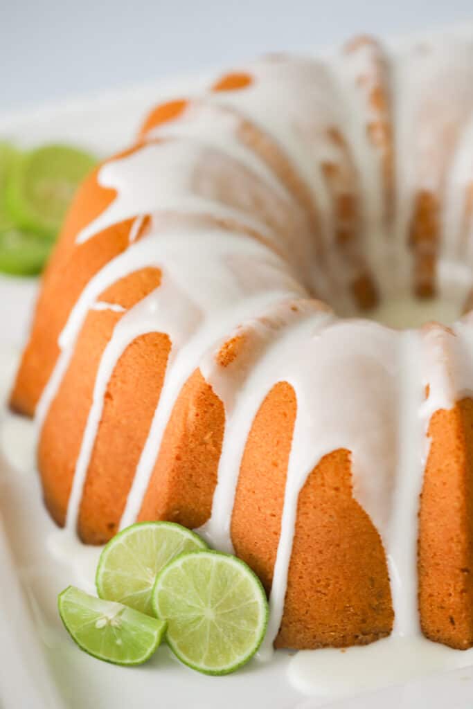 A full pound cake baked in a bundt cake pan, topped with white glaze with fresh slices of lime on the side.key lime pound cake recipes. key lime cake recipe, 