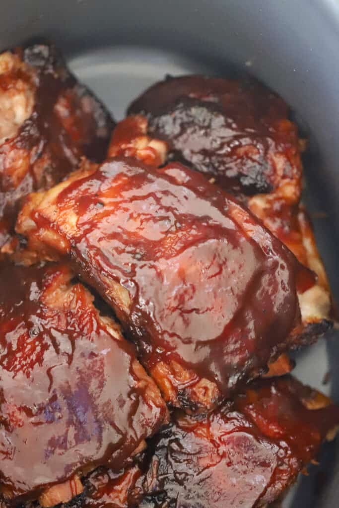 Cooked spare ribs covered in BBQ sauce in the bottom of a slow cooker.
