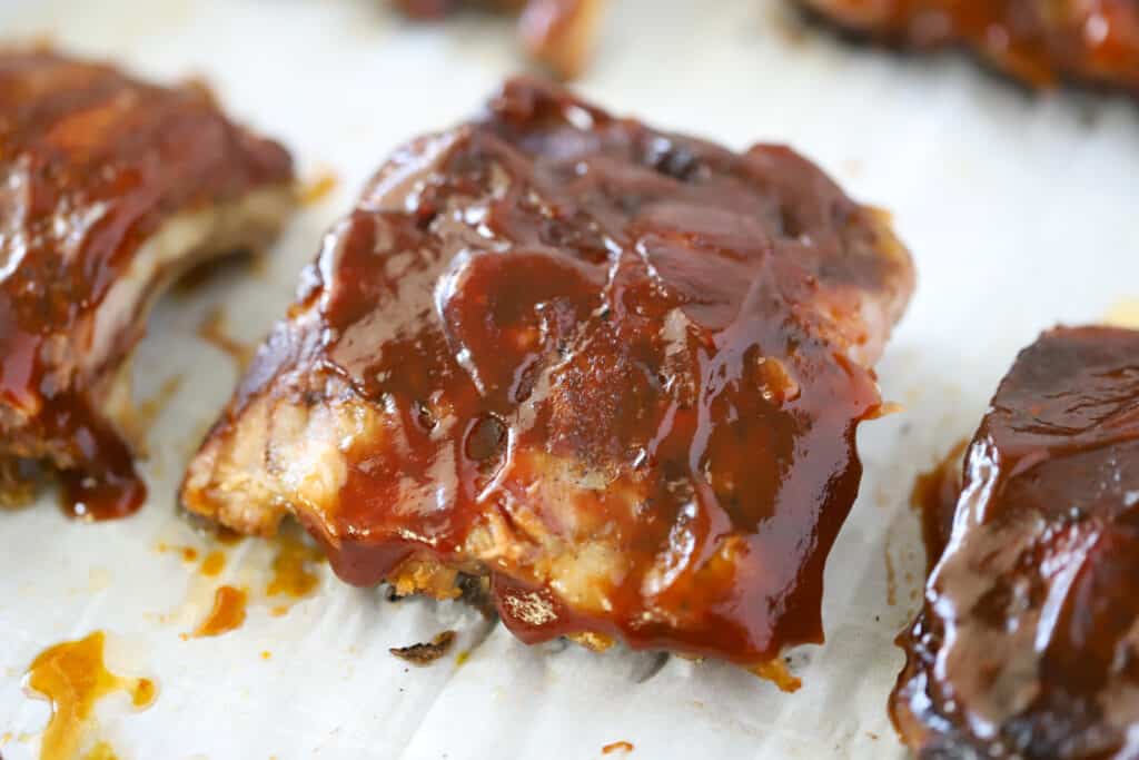 Slow Cooker BBQ Spare Ribs covered in sauce and resting on a sheet tray.