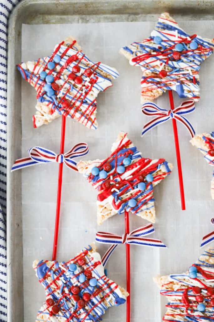 Star shaped 4th of July treats on a sheet tray made from Rice Krispie Treats, stuck with sticks and decorated with red white and blue chocolate candies.   crispy pop. 