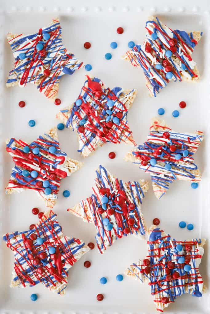 A serving platter full of Rice Krispie Treats cut into star shapes and decorated with red, white and blue chocolate and candies.