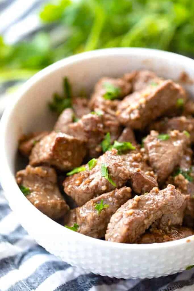 A white bowl full of garlic butter steak bites served with delicious steak bite sauce.