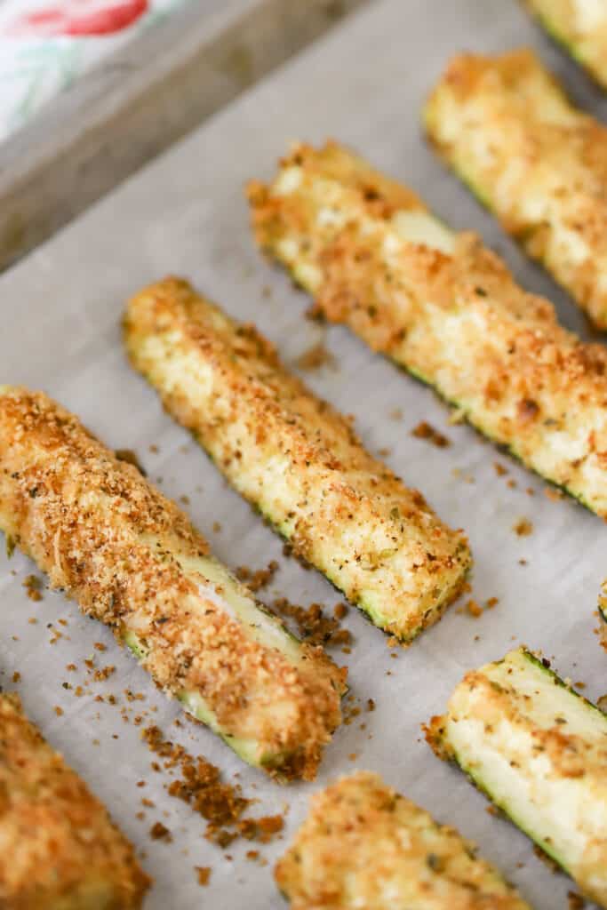 A sheet tray covered with parchment paper with panko crusted Zucchini Fries lined up. Zucchini sticks.