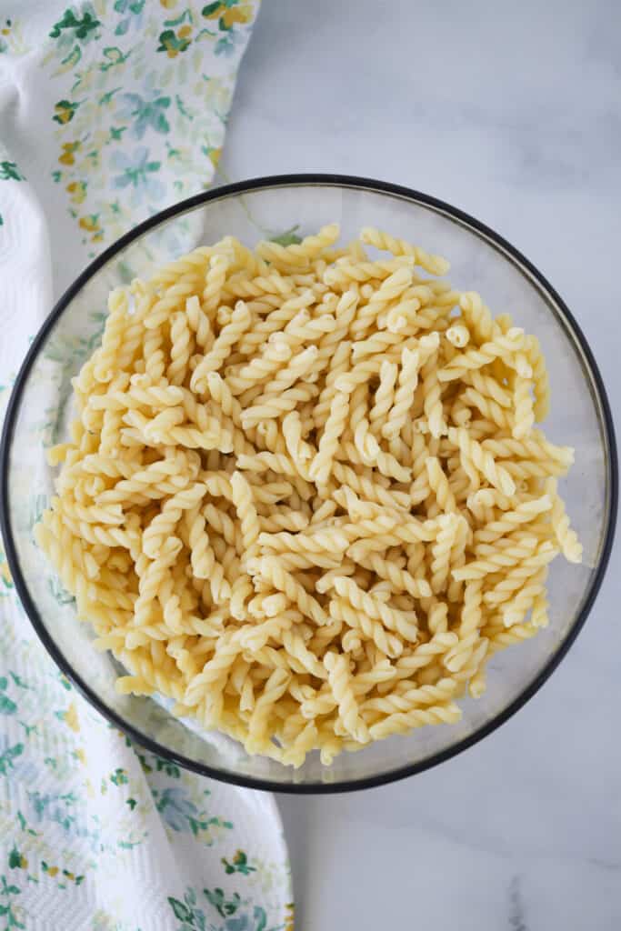 A large glass bowl full of cooked spiral pasta noodles.