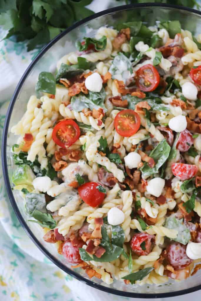 Pasta salad in a large glass serving bowl filled with bacon, lettuce and tomatoes.