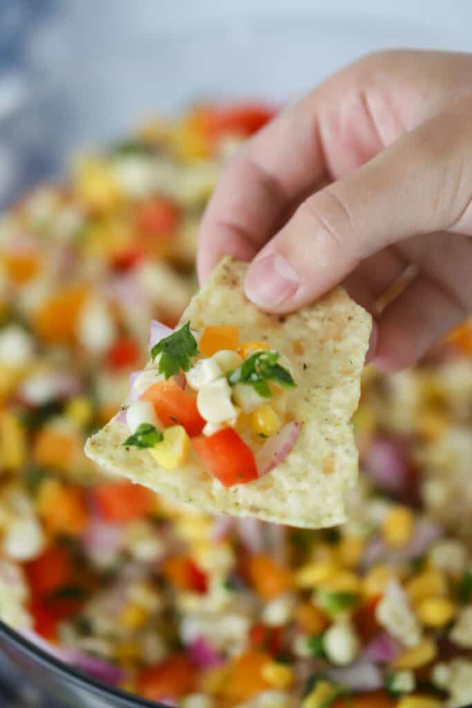 A hand holding a chip with Corn Salsa on it; easy corn salsa; corn appetizer; canned corn salsa recipe.