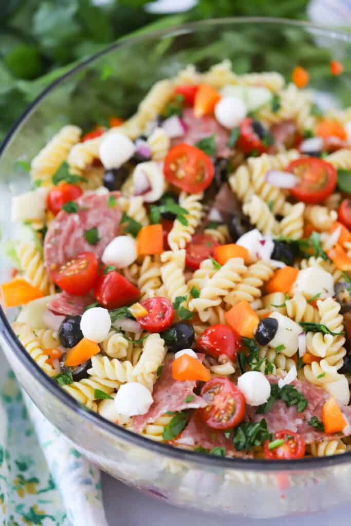 A large glass serving bowl full of cold pasta salad.