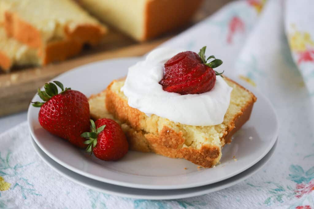 A small white plate with two slices of pound cake topped with whipped cream and fresh strawberries.