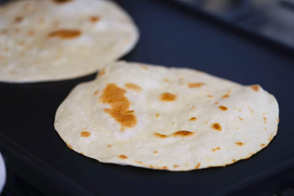 Two large flour tortillas cooking on a flat skillet.