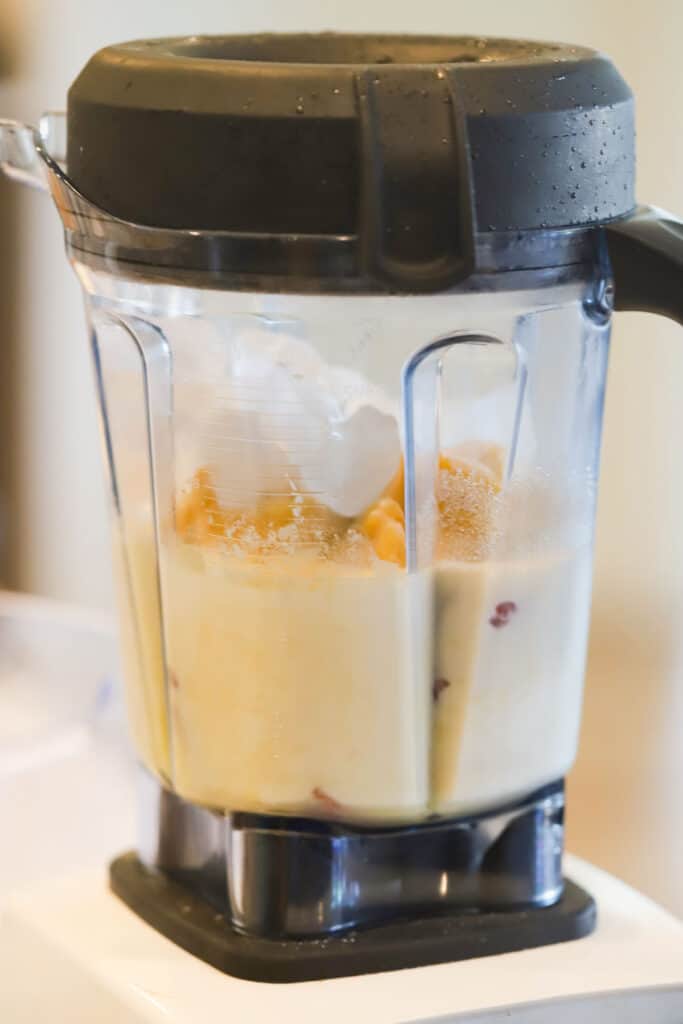 A side view of a blender filled with ingredients to make this Strawberry Orange Julius recipe. how to make an orange julius, orange julius recipe with orange juice